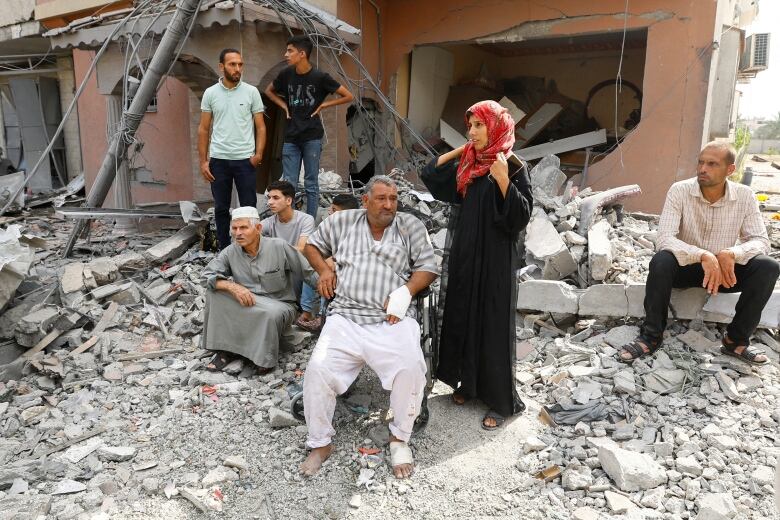 Group of people stand and sit amidst rubble. 