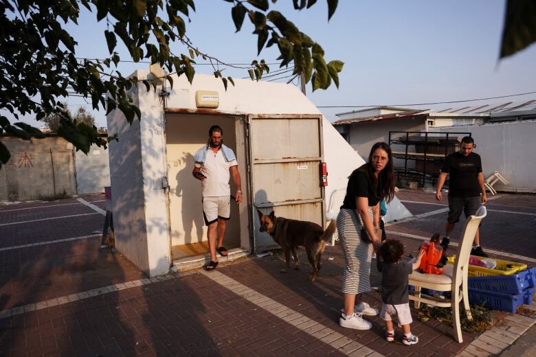 Three adults, one child, and one dog, gather by the opening of a bomb shelter door. 