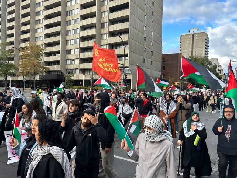 A crowd of protesters marches through the streets of Montreal waving Palestinian flag. 