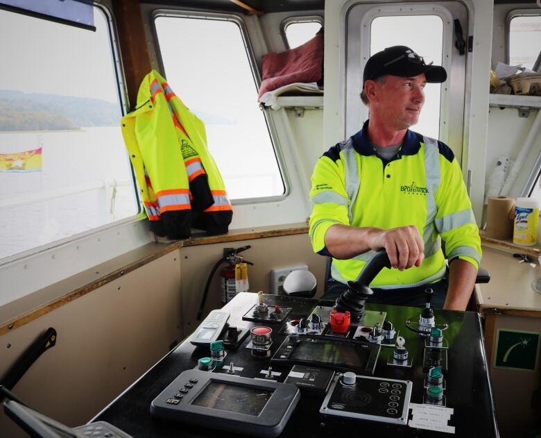 A department of transportation ferry worker sits on the bridge of a cable ferry, scanning the horizon. 