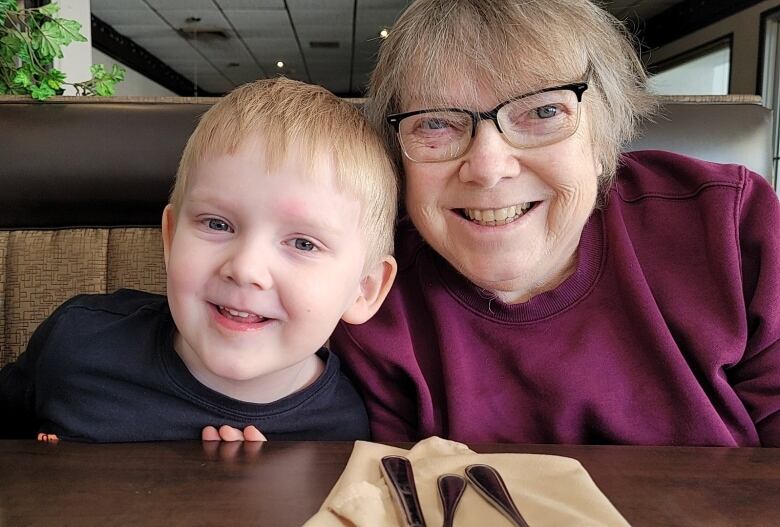 A close of portrait of a young boy and an older woman, both smiling, who are sitting at a table. 