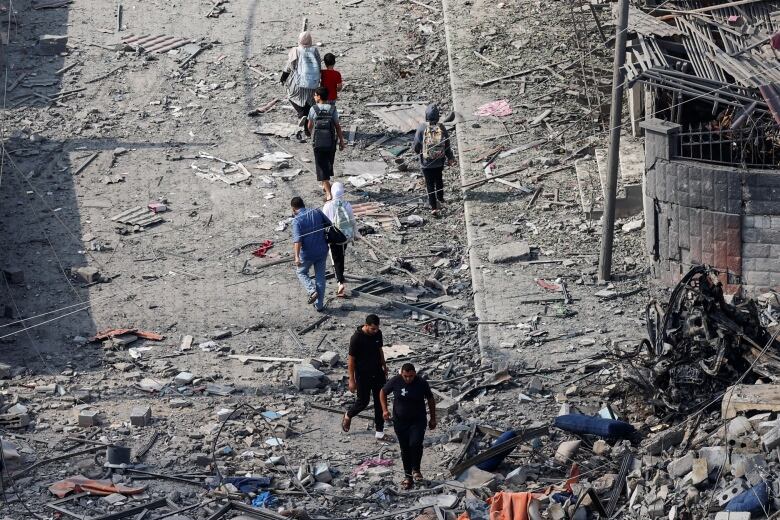 People walk through rubble of destroyed buildings