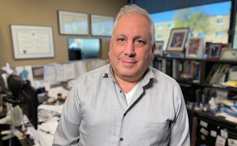 A man in a grey button down shirt poses for a photo. 