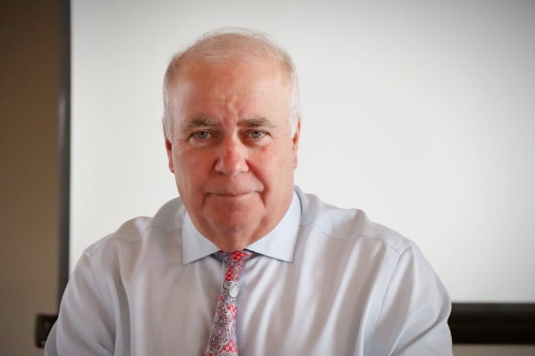 A man with a white shirt and print tie smiles for the camera.