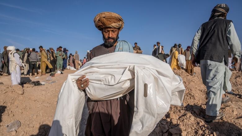 A man in a turban cradles a plastic sheet with a body inside.