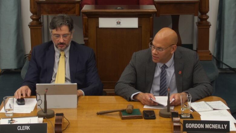 Two men sit behind a desk.