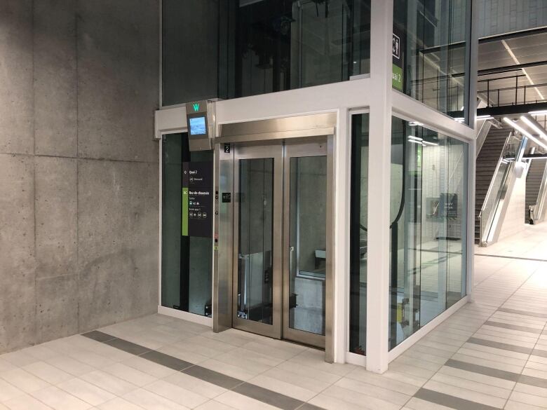 Shiny glass elevator with stone floors and walls around it.