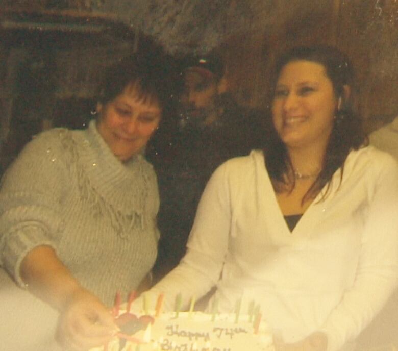 Teri-Lynn Wilson, left, holds a birthday cake while another woman lights candles on it.