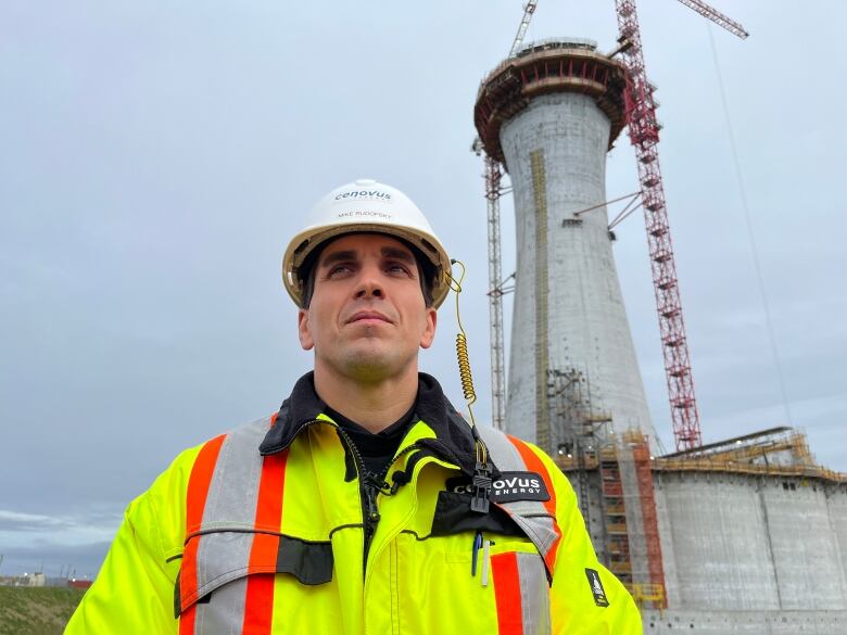 A man clad in personal protective equipment stands in front of a massive concrete structure that will form the base of a oil project called the West White Rose project.