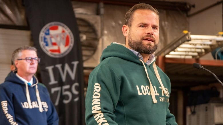 A man wearing a dark green hoodie stands at a podium.