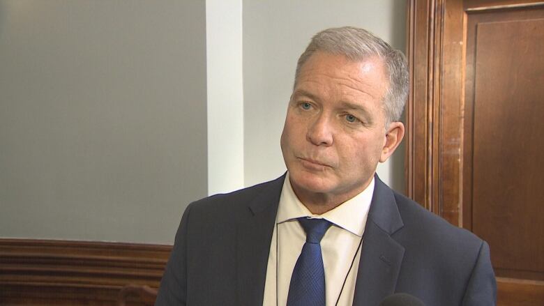 A man with grey hair wears a suit and looks off camera. 