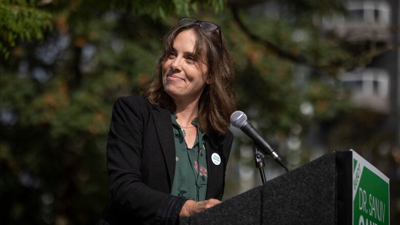 A white woman speaks at a podium while wearing green.