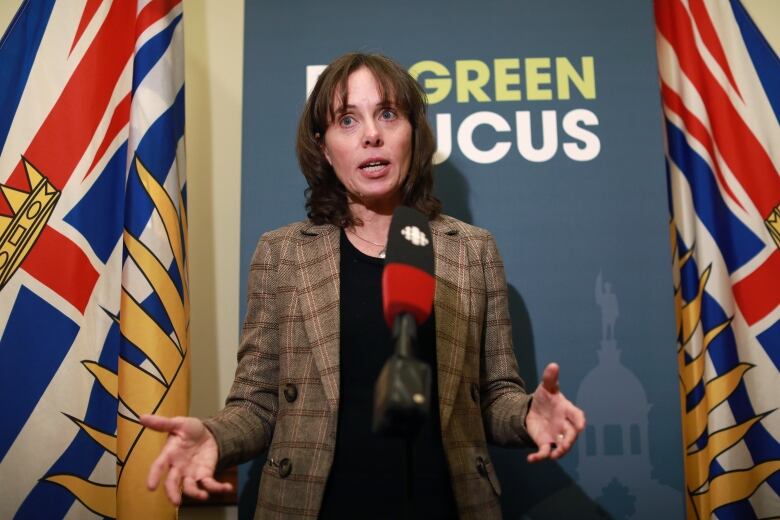 A white woman speaks in front of a banner titled 'Green Caucus'.