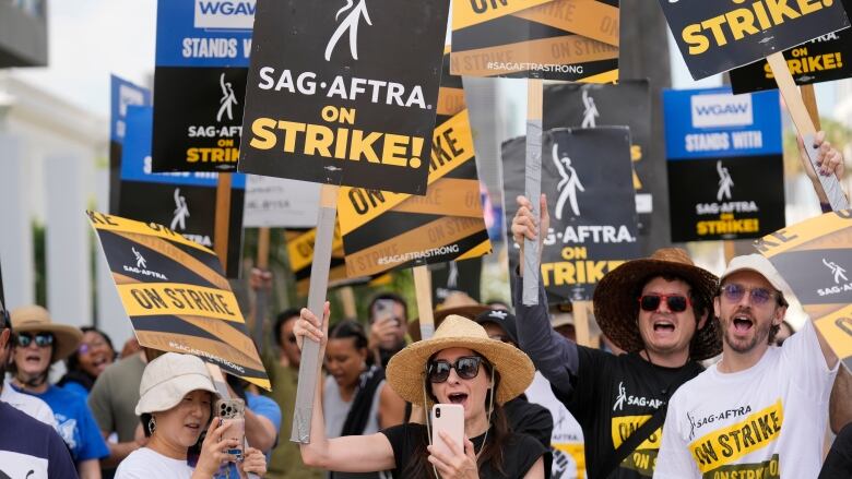 Striking Hollywood actors hold signs as they picket.