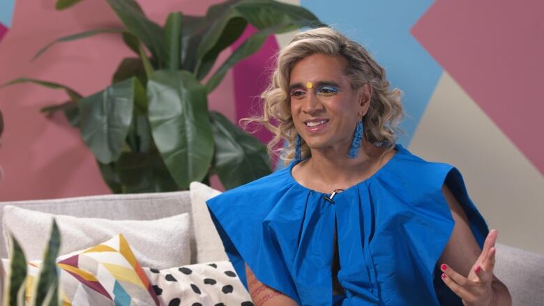 Vivek Shraya sitting down on a couch on the set of Here & Queer.