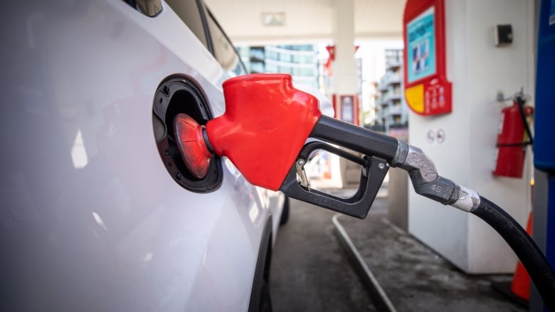 A gas nozzle sticks out of the gas tank of a white vehicle.