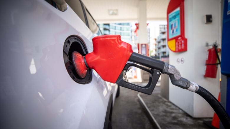 A gas nozzle sticks out of the gas tank of a white vehicle.