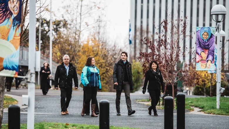 Group of people walking on leafy concrete path. 