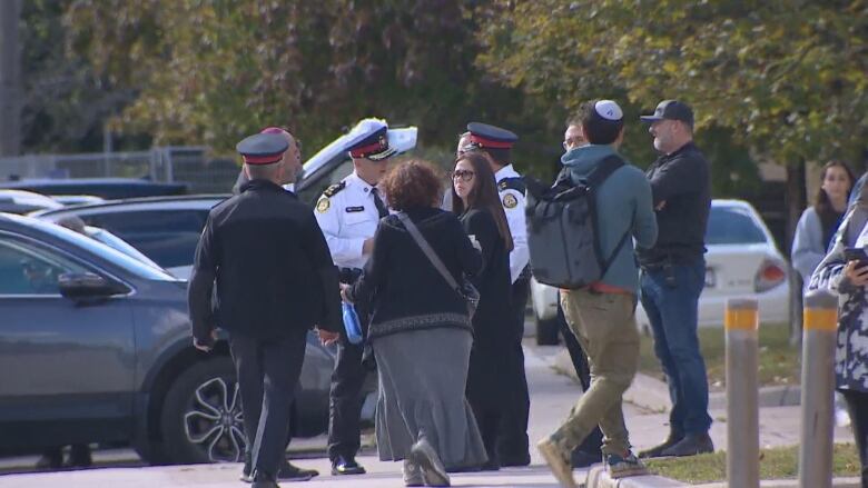 Police officers speak to people near a parking lot.