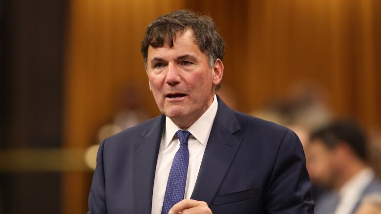 A man in a navy blue suit and tie stands in the House of Commons.