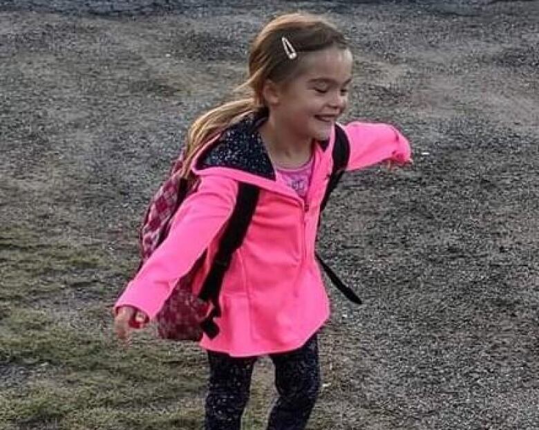 A little girl, wearing pink, smiling with her arms outstretched