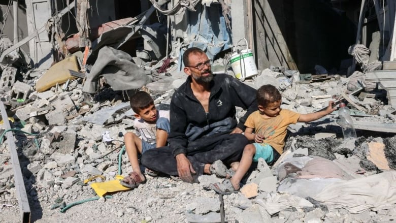 A man and his two sons sit outside a building destroyed in an airstrike.