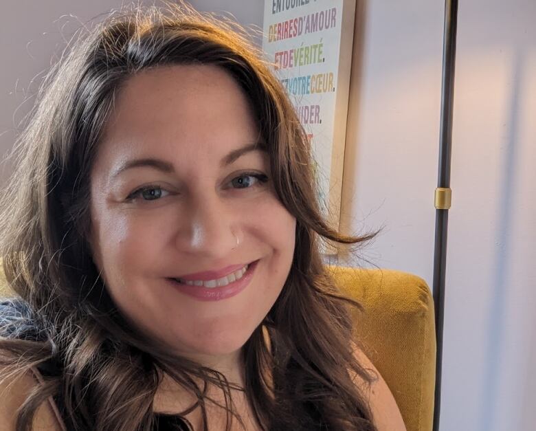 A selfie of a smiling woman with long, wavy brown hair.