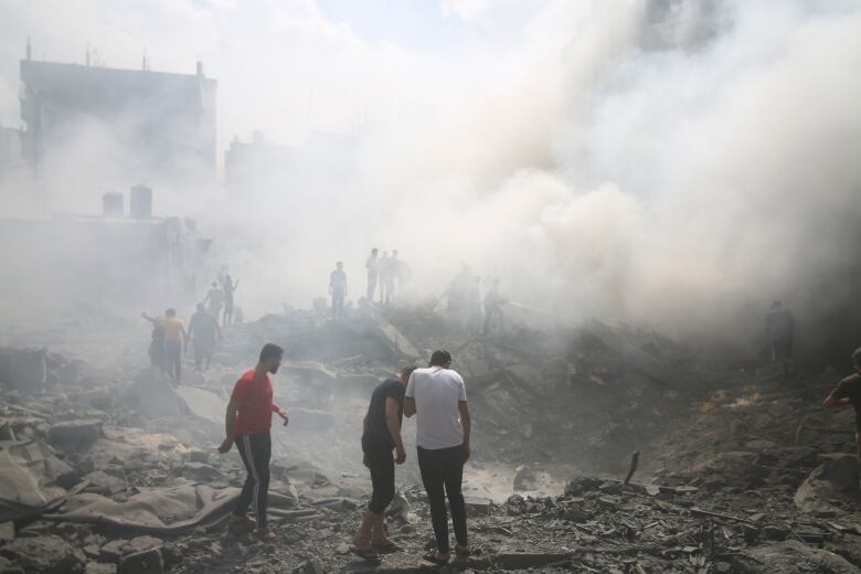 People stand in a dust cloud amid rubble.