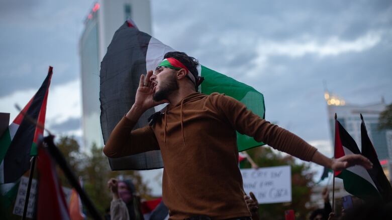 A man seems to shout standing in front of a Palestinian flag