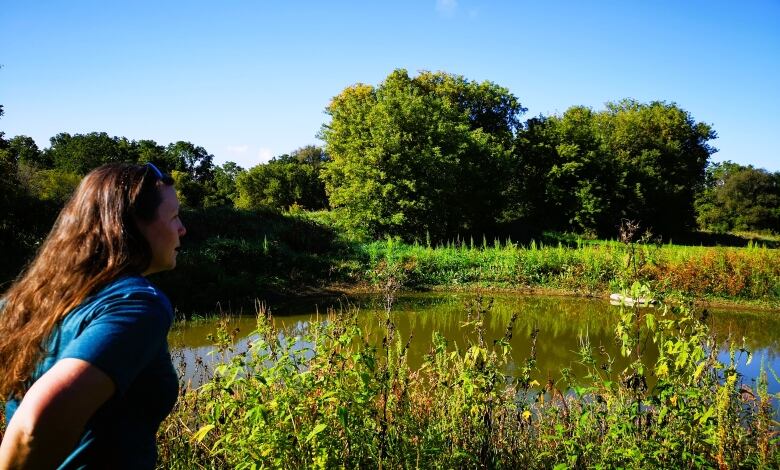 A woman in a blue shirt looks out, over a pond