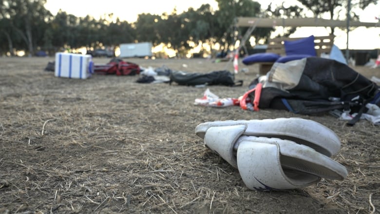 A white sandal is show in  the foreground of a field filled with scattered camping equipment.