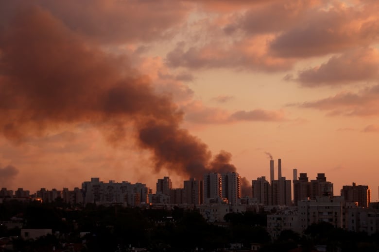 Smoke rises in the distance over a city skyline.