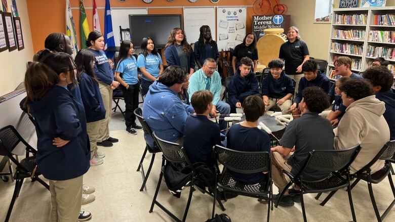 young people, dressed in matching dark shirts, gather around some young boys who are singing around a big drum.