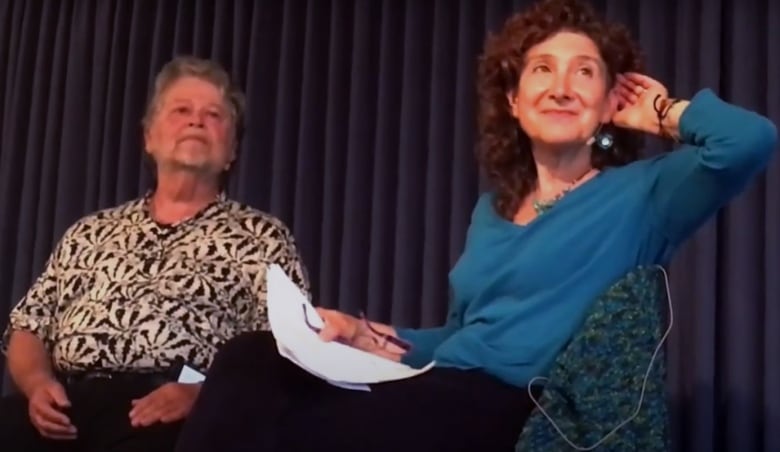 A screenshot taken from a YouTube video shows an older white couple sitting on stage.