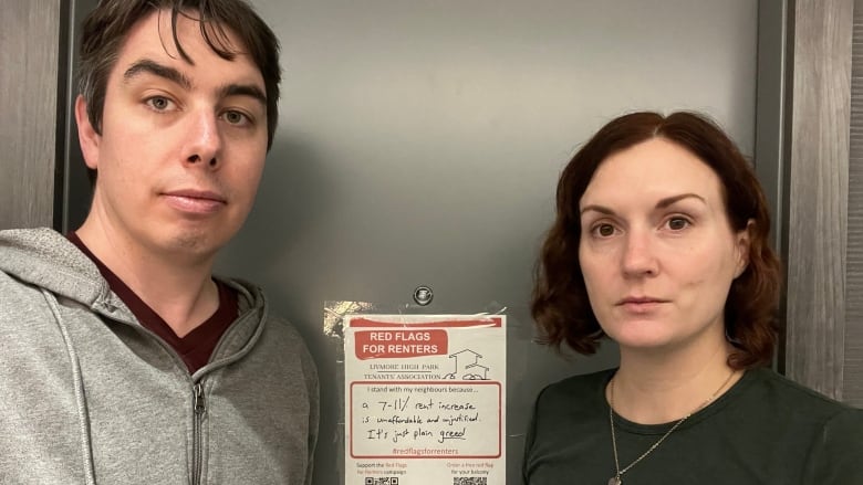 Two people stand in front of a door with a sign on it.