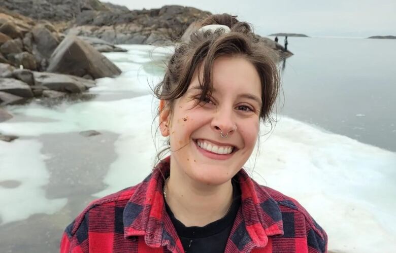 A woman wearing a plaid jacket smiles and looks at the camera with the sea ice in the background. 