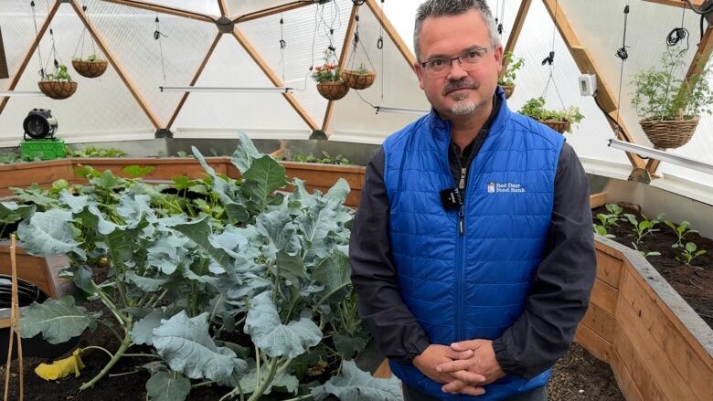 Mitch Thomson stands by planters full of vegetables inside a domed greenhouse.