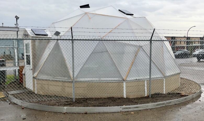 A futuristic looking greenhouse stands behind a security fence in Red Deer.