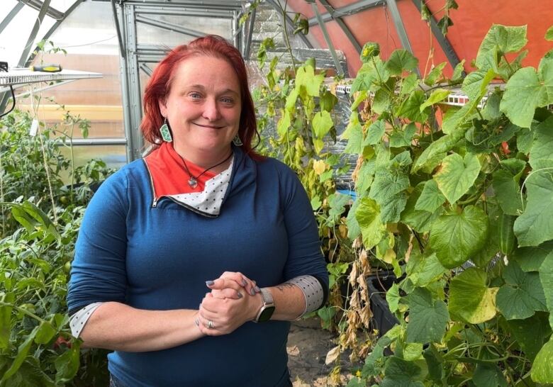 Raygan Solotki stands in a research greenhouse surrounded by green leaves and vegetables.