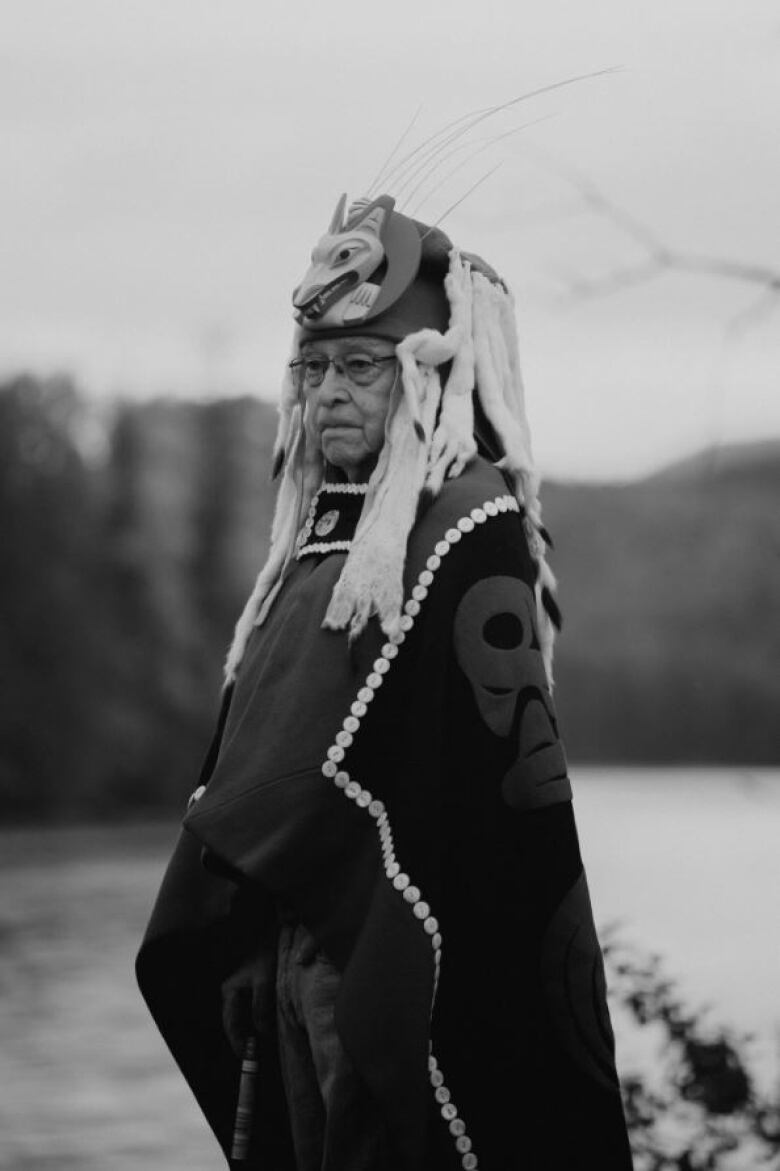 In a black and white photo, a First Nations chief is shown in traditional regalia.