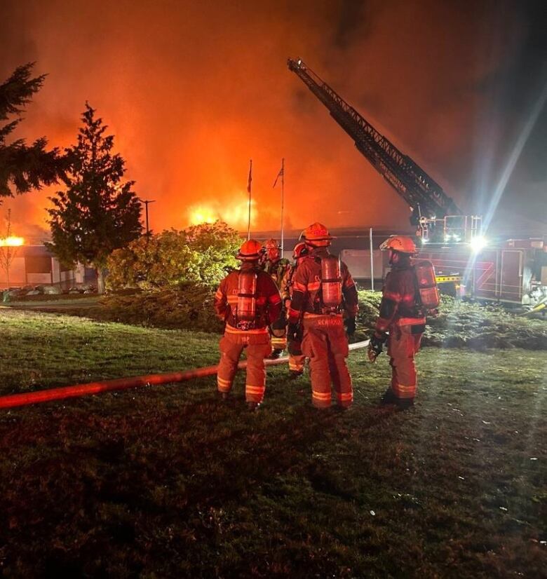 Firefighters stand in front of a burning building.