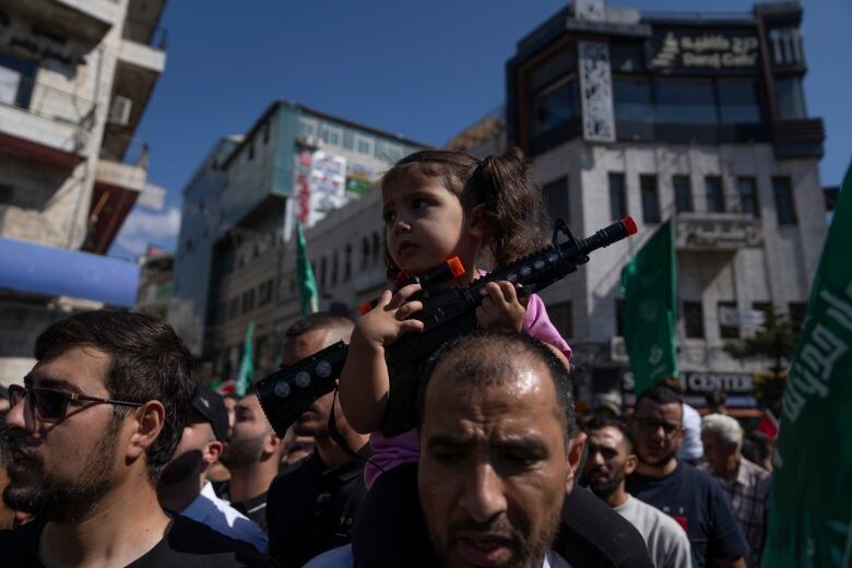 A girl holding a toy gun sits on a man's shoulders.