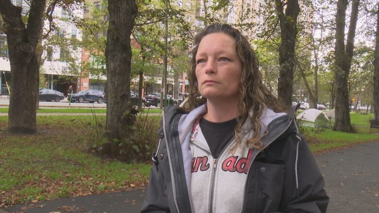 A woman in a zipped hoodie speaks to the camera.