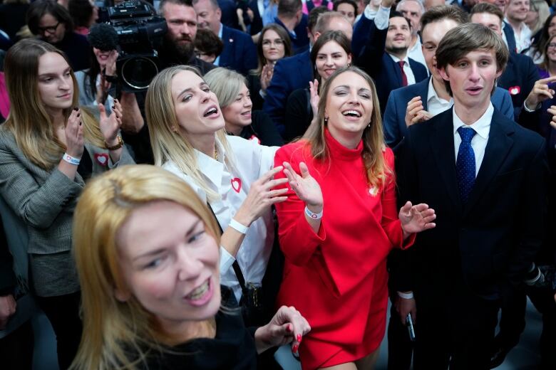 People in a crowd are seen clapping hands and cheering.