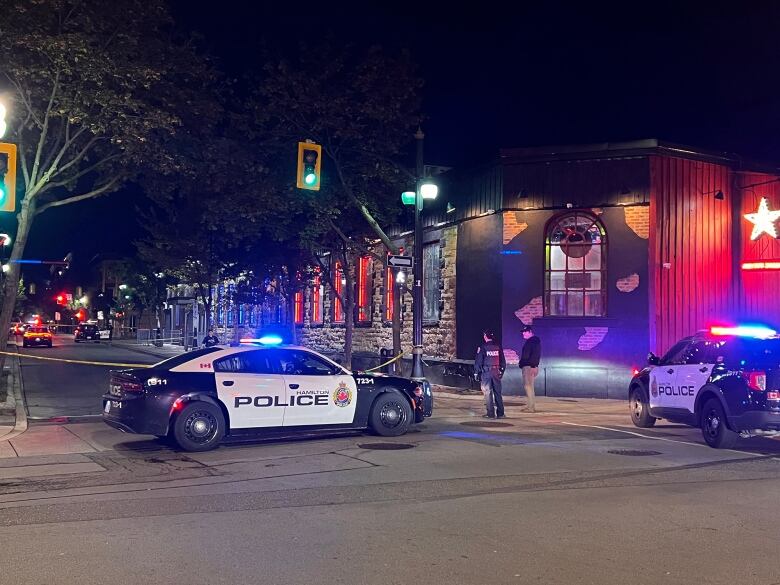 Hamilton police officers stand near police tape and two police cars outside a Hamilton nightclub where two men were shot.