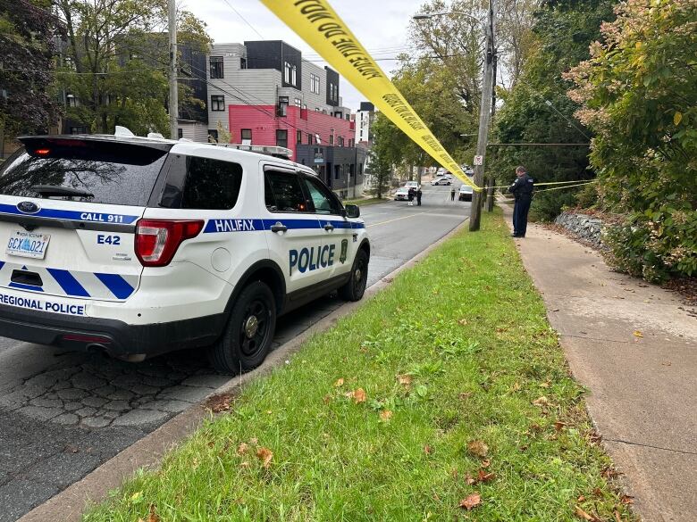 Yellow police tape and a white and blue police vehicle are shown on a street.