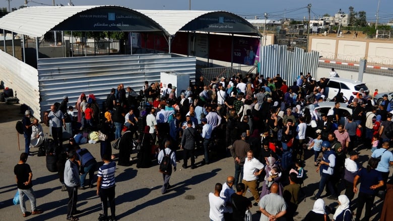 A large crowd gathers in front of a border crossing.