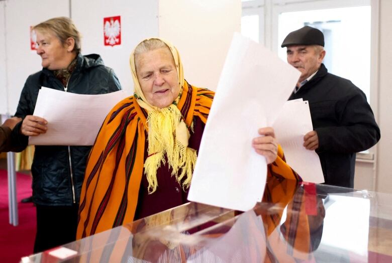 A person puts a large paper into a clear box as other people stand behind them.