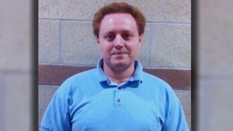 A man in a blue polo shirt poses against a concrete wall.