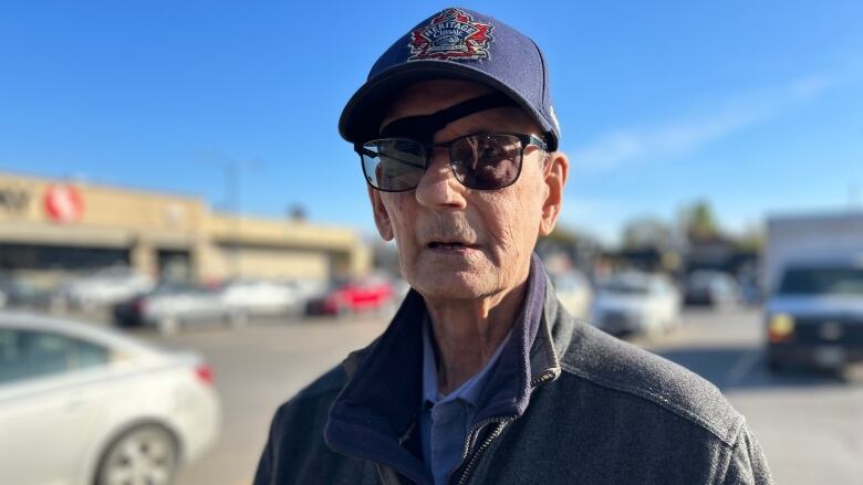 A man wearing a baseball hat and glasses is standing in a parking lot.